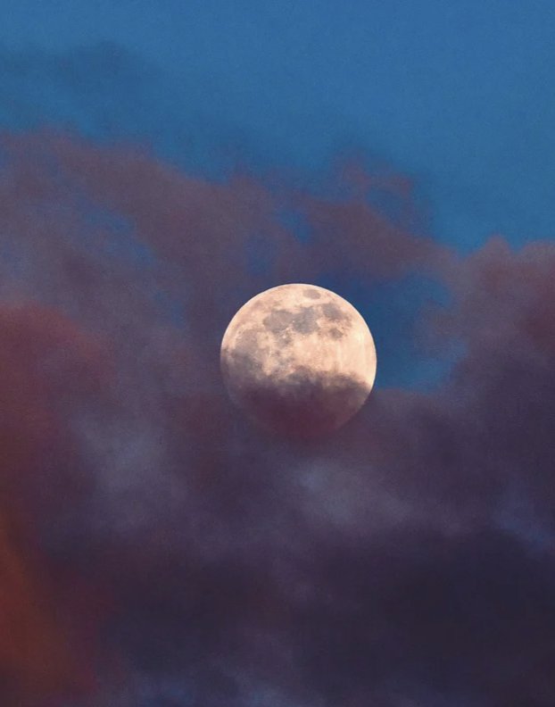 The moon glowing through clouds at dusk